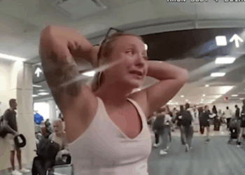 Una mujer con las manos en la cabeza, llorando, mientras otros caminan en una terminal de aeropuerto.