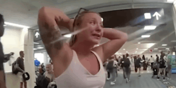 Una mujer con las manos en la cabeza, llorando, mientras otros caminan en una terminal de aeropuerto.