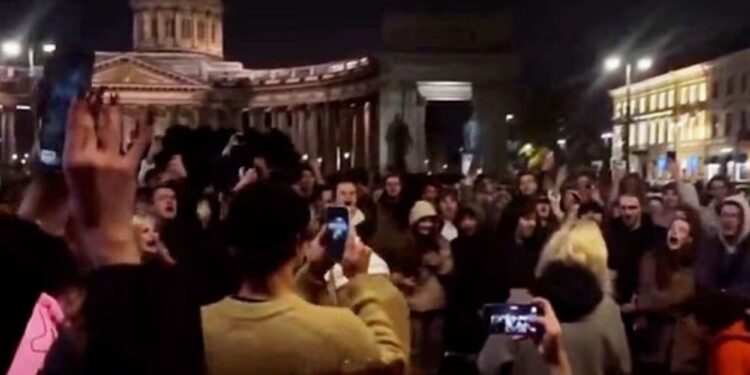 Un collage de imágenes que contiene 1 imágenes. La imagen 1 muestra una multitud de personas filmando un concierto nocturno frente a la Catedral de Kazán.