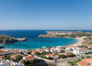 Arenal d'en Castell, Menorca, España con casas con vistas a una playa y una cala turquesa.
