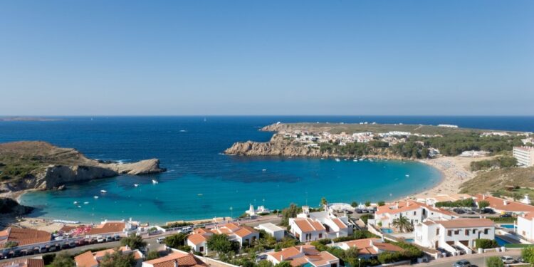 Arenal d'en Castell, Menorca, España con casas con vistas a una playa y una cala turquesa.