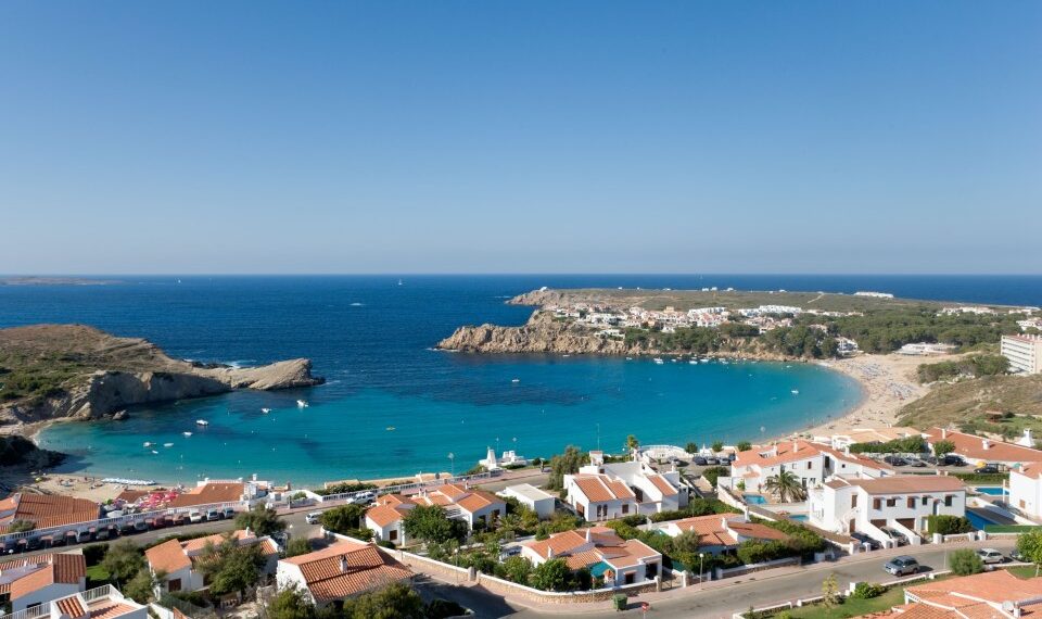 Arenal d'en Castell, Menorca, España con casas con vistas a una playa y una cala turquesa.