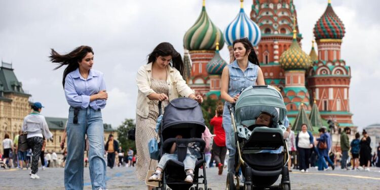 Tres mujeres empujando cochecitos para bebés en la Plaza Roja con la Catedral de San Basilio en el fondo.