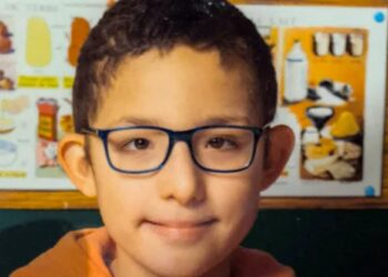 Un collage de imágenes que contiene 1 imagen. La imagen 1 muestra una foto de la cabeza de Rayan, un niño de 13 años con cabello oscuro y gafas azules, que lleva una sudadera con capucha naranja.