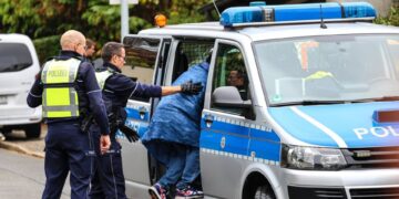Agentes de policía metiendo a un adolescente en un coche de policía.