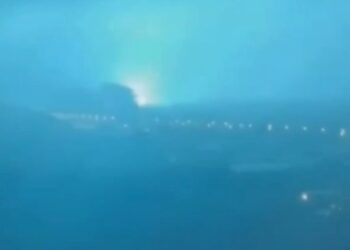 Horizonte de la ciudad por la noche con un brillante destello de luz azul-verde en la distancia.