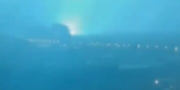 Horizonte de la ciudad por la noche con un brillante destello de luz azul-verde en la distancia.