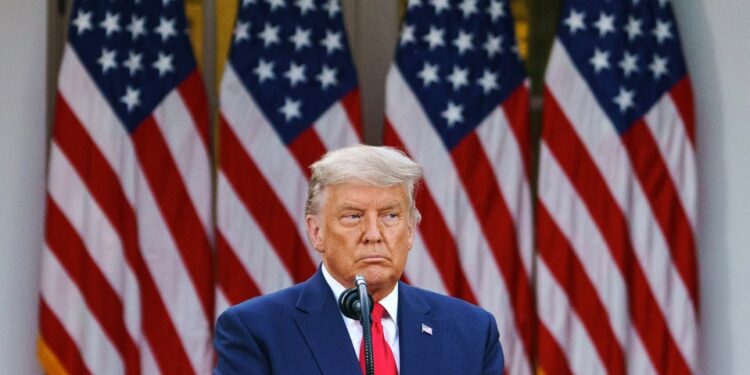 Donald Trump hablando en un podio frente a cuatro banderas estadounidenses.