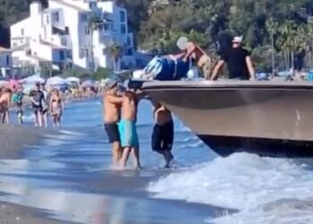 Los traficantes de drogas descargan drogas de un bote en una playa llena de gente.
