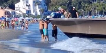 Los traficantes de drogas descargan drogas de un bote en una playa llena de gente.