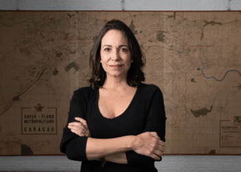 Mujer de cabello oscuro y top negro parada frente a un mapa antiguo de Caracas.