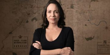 Mujer de cabello oscuro y top negro parada frente a un mapa antiguo de Caracas.