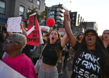 Los manifestantes se toman de la mano y gritan consignas mientras caminan por la calle U durante una protesta. "Poner fin a la ocupación de DC" Manifestación contra el presidente estadounidense Donald Trump y su uso de poderes de emergencia para hacerse cargo de la policía de D.C. en Washington, DC, el 23 de agosto de 2025.