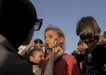 Un voluntario pinta la cara de una niña mientras los niños se reúnen entre los edificios destruidos en el campo de refugiados de Al Shati en la ciudad de Gaza, Gaza, el 23 de noviembre de 2025.