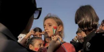 Un voluntario pinta la cara de una niña mientras los niños se reúnen entre los edificios destruidos en el campo de refugiados de Al Shati en la ciudad de Gaza, Gaza, el 23 de noviembre de 2025.