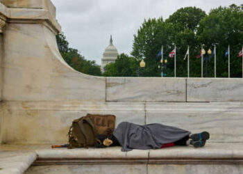 Una persona sin hogar duerme en un banco con el edificio del Capitolio de Estados Unidos al fondo.