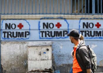 Una pareja pasa junto a un graffiti contra el presidente estadounidense Donald Trump el 26 de marzo de 2020 en Caracas, Venezuela.