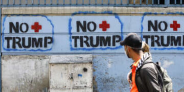 Una pareja pasa junto a un graffiti contra el presidente estadounidense Donald Trump el 26 de marzo de 2020 en Caracas, Venezuela.