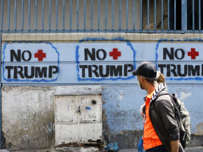 Una pareja pasa junto a un graffiti contra el presidente estadounidense Donald Trump el 26 de marzo de 2020 en Caracas, Venezuela.