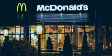 Un collage de imágenes que contiene 1 imagen. La imagen 1 muestra el letrero del restaurante McDonald's iluminado por la noche.