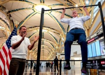 El influyente Dr. Paul Saladino observa al Secretario de Transporte, Sean P. Duffy, hacer flexiones después de una conferencia de prensa sobre el lanzamiento del "Haga que los viajes vuelvan a ser familiares" Campaña en el Aeropuerto Nacional Ronald Reagan de Washington en Arlington, Virginia, el 8 de diciembre de 2025. (Heather Diehl/Getty Images)