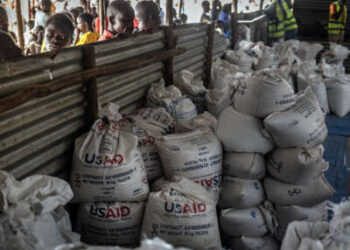 Refugiados congoleños miran a través de una valla de metal corrugado los últimos lotes de alimentos entregados por la ahora desmantelada Agencia de los Estados Unidos para el Desarrollo Internacional (USAID) en un área de almacenamiento y entrega de alimentos en el sitio de refugiados de Musenyi en Giharo, el 7 de mayo de 2025.