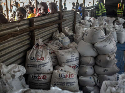 Refugiados congoleños miran a través de una valla de metal corrugado los últimos lotes de alimentos entregados por la ahora desmantelada Agencia de los Estados Unidos para el Desarrollo Internacional (USAID) en un área de almacenamiento y entrega de alimentos en el sitio de refugiados de Musenyi en Giharo, el 7 de mayo de 2025.
