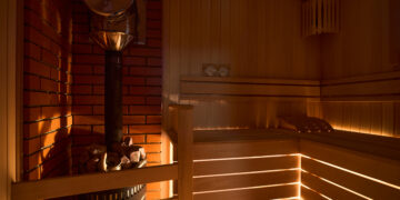 Casa de baños de sauna rusa con luz íntima y tenue desde debajo del banco, linterna de madera, termómetro higrómetro con estufa de sauna, horno con calentador interno de piedra y piedras y chimenea o tubería.