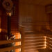 Casa de baños de sauna rusa con luz íntima y tenue desde debajo del banco, linterna de madera, termómetro higrómetro con estufa de sauna, horno con calentador interno de piedra y piedras y chimenea o tubería.