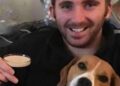 Hombre sonriendo y sosteniendo una pinta de cerveza con un beagle a su lado.