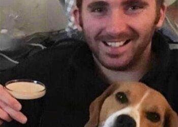 Hombre sonriendo y sosteniendo una pinta de cerveza con un beagle a su lado.