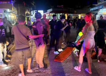 Un collage de imágenes que contiene 1 imagen. La imagen 1 muestra que los paramédicos y la policía atienden a una víctima en una calle por la noche.
