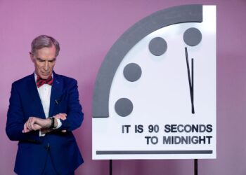 Un collage de imágenes que contiene 1 imagen. La imagen 1 muestra al educador científico Bill Nye mirando su reloj junto al "Reloj del fin del mundo" establecido en 90 segundos para la medianoche