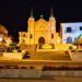 Un collage de imágenes que contiene 1 imágenes. La imagen 1 muestra la vista nocturna de la Capilla de Santa Vera Cruz en Alhaurín El Grande, provincia de Málaga, España, que presenta una torre única de tres secciones y una estructura triangular.