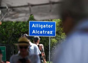 Las personas alrededor de un letrero de Alligator Alcatraz aparecen borrosas mientras el letrero permanece enfocado.
