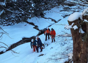 Cuatro personas con ropa de invierno y cascos navegando por un paisaje cubierto de nieve junto a un arroyo helado.