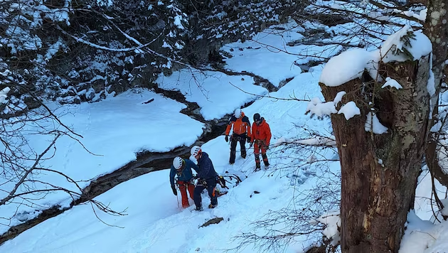 Cuatro personas con ropa de invierno y cascos navegando por un paisaje cubierto de nieve junto a un arroyo helado.