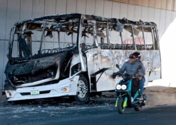 Una motocicleta pasa junto a un autobús quemado utilizado para bloquear una avenida en Tonalá, Jalisco, México, el 23 de febrero de 2026. (Ulises Ruiz/AFP vía Getty Images)