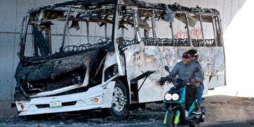Una motocicleta pasa junto a un autobús quemado utilizado para bloquear una avenida en Tonalá, Jalisco, México, el 23 de febrero de 2026. (Ulises Ruiz/AFP vía Getty Images)