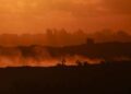 Esta fotografía tomada desde una posición en la frontera israelí con la Franja de Gaza muestra la puesta de sol detrás de edificios destruidos mientras las excavadoras israelíes trabajan en medio de un alto el fuego entre las facciones israelíes y palestinas en el territorio asediado el 14 de octubre de 2025.