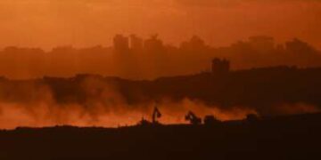 Esta fotografía tomada desde una posición en la frontera israelí con la Franja de Gaza muestra la puesta de sol detrás de edificios destruidos mientras las excavadoras israelíes trabajan en medio de un alto el fuego entre las facciones israelíes y palestinas en el territorio asediado el 14 de octubre de 2025.
