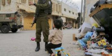 Un soldado israelí armado habla con un niño mientras otros soldados hacen guardia en la ciudad vieja de Hebrón, en la ocupada Cisjordania, el 6 de diciembre de 2025. La zona está asegurada habitualmente por tropas para permitir que los colonos israelíes recorran la ciudad.