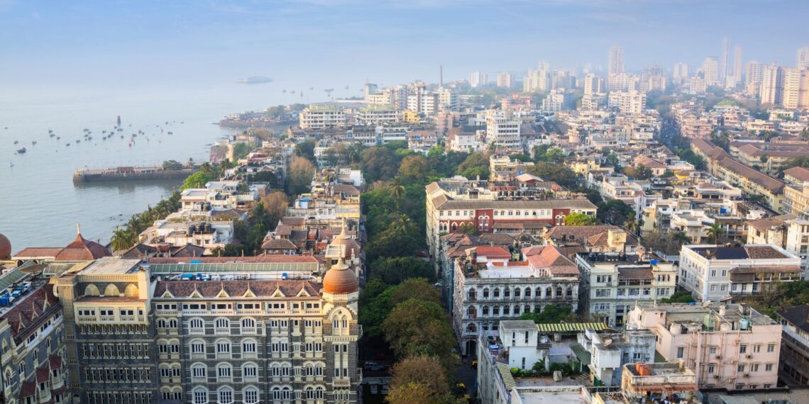 Un collage de imágenes que contiene 1 imagen. La imagen 1 muestra una vista aérea de la ciudad de Mumbai y el hotel Taj Mahal Palace junto al Mar Arábigo.