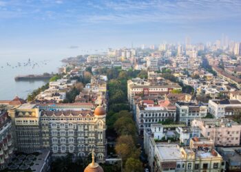 Un collage de imágenes que contiene 1 imagen. La imagen 1 muestra una vista aérea de la ciudad de Mumbai y el hotel Taj Mahal Palace junto al Mar Arábigo.