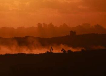 Esta fotografía tomada desde una posición en la frontera israelí con la Franja de Gaza muestra la puesta de sol detrás de edificios destruidos mientras las excavadoras israelíes trabajan en medio de un alto el fuego entre las facciones israelíes y palestinas en el territorio asediado el 14 de octubre de 2025.