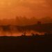 Esta fotografía tomada desde una posición en la frontera israelí con la Franja de Gaza muestra la puesta de sol detrás de edificios destruidos mientras las excavadoras israelíes trabajan en medio de un alto el fuego entre las facciones israelíes y palestinas en el territorio asediado el 14 de octubre de 2025.