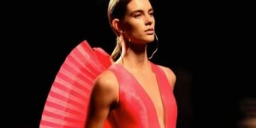 Un collage de imágenes que contiene 1 imágenes. La imagen 1 muestra una modelo con cabello castaño claro, que lleva un vestido rosa brillante con un escote en V pronunciado y un detalle plisado en forma de abanico en los hombros, de pie contra un fondo oscuro.