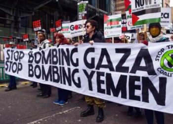 La gente marcha detrás de una pancarta que dice "DEJEN DE BOMBARDEAR GAZA; DEJEN DE BOMBARDEAR YEMEN" durante una protesta al aire libre