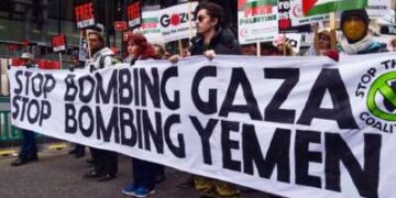 La gente marcha detrás de una pancarta que dice "DEJEN DE BOMBARDEAR GAZA; DEJEN DE BOMBARDEAR YEMEN" durante una protesta al aire libre
