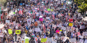 Personas ondeando banderas y portando carteles llenan una calle durante la protesta No Kings